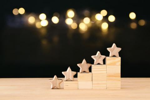 Wooden stars on stepped blocks from lowest to highest. Blurred lights are in the background